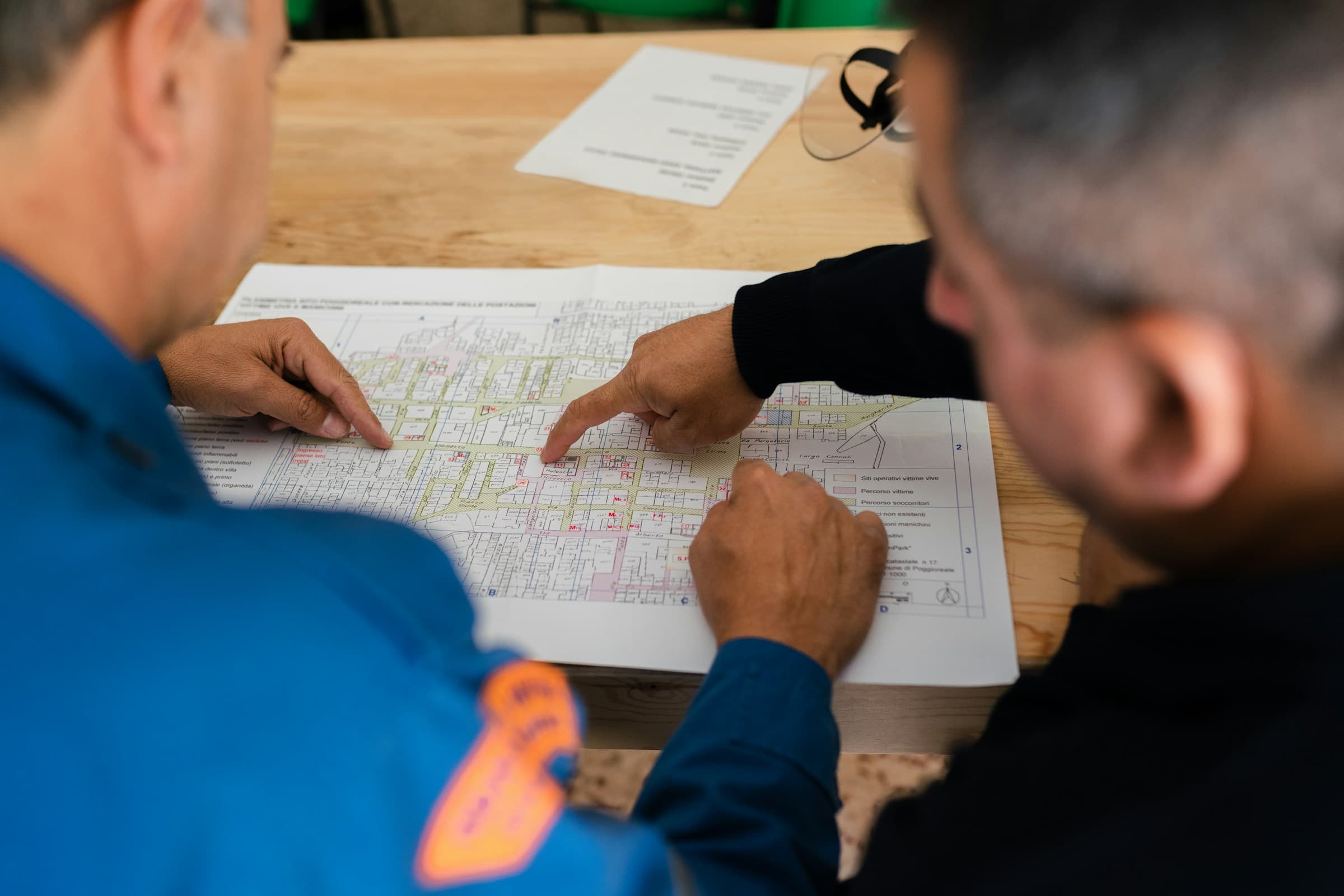 Two people in work uniforms reviewing a printed technical drawing on a table, pointing at details